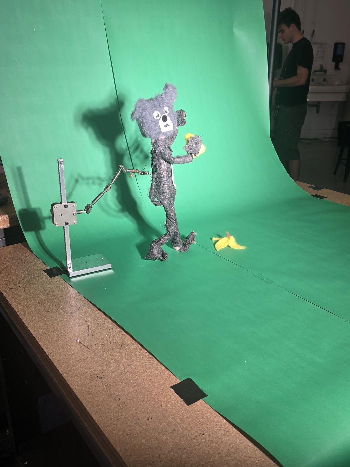 The mouse puppet on a rig stand in front of a green screen, with the banana peel on the floor